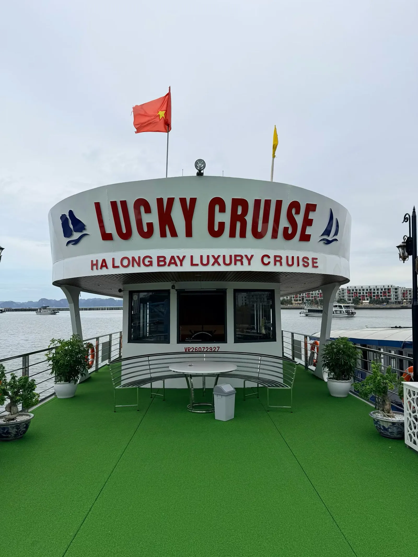 The deck of a Ha Long Bay cruise boat, with green artificial turf and a cabin bearing a LUCKY CRUISE sign beneath a flying Vietnamese flag