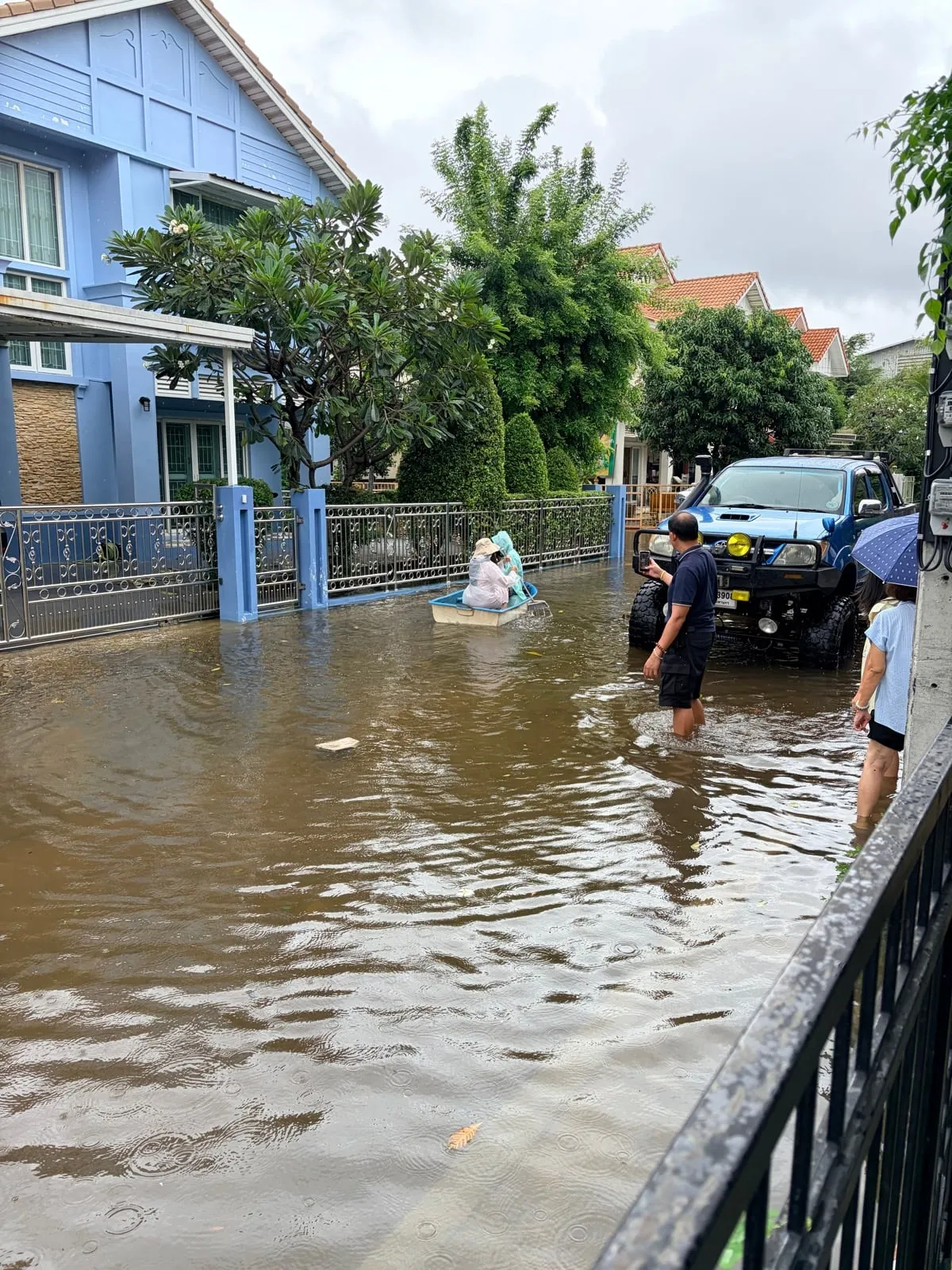 A flooded neighbourhood road, with a small boat and a pickup outside the gate